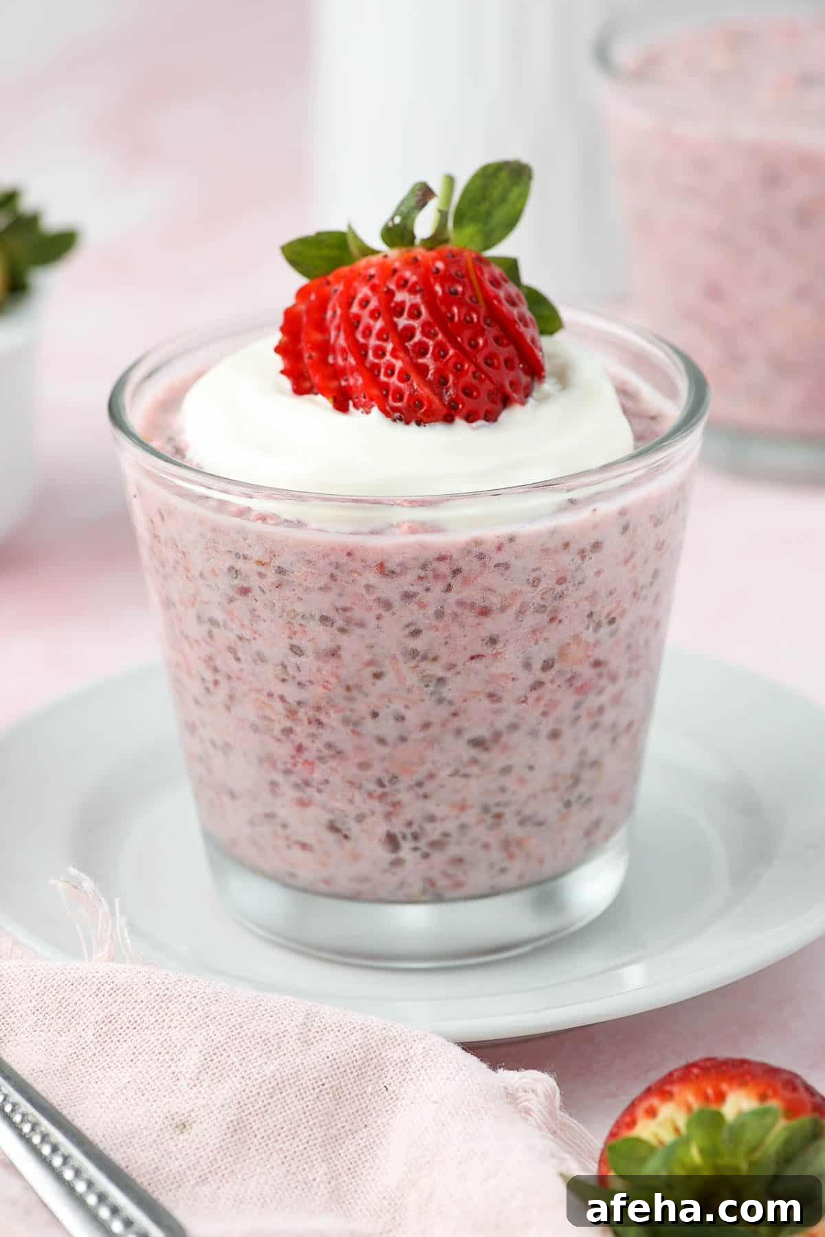 Glass jar of strawberry overnight oats, topped with yoghurt and a strawberry, sitting on a white saucer.