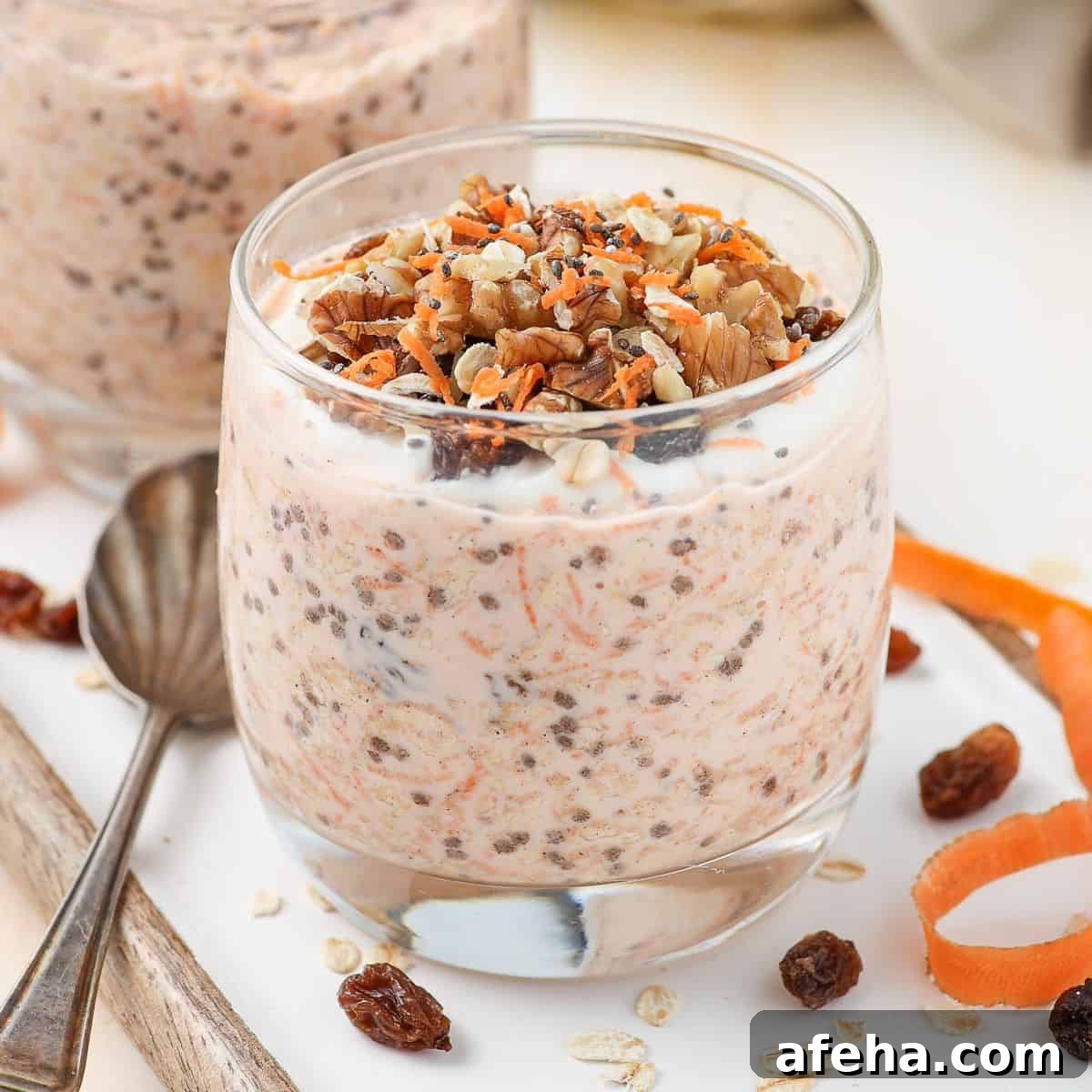 Glass of overnight oats garnished with walnuts and grated carrot, sitting on board with a spoon on the edge.