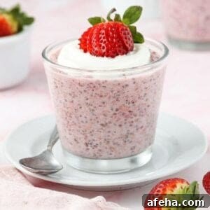 Glass jar of strawberry overnight oats, topped with yoghurt and a strawberry, sitting on a white saucer with a spoon on edge.