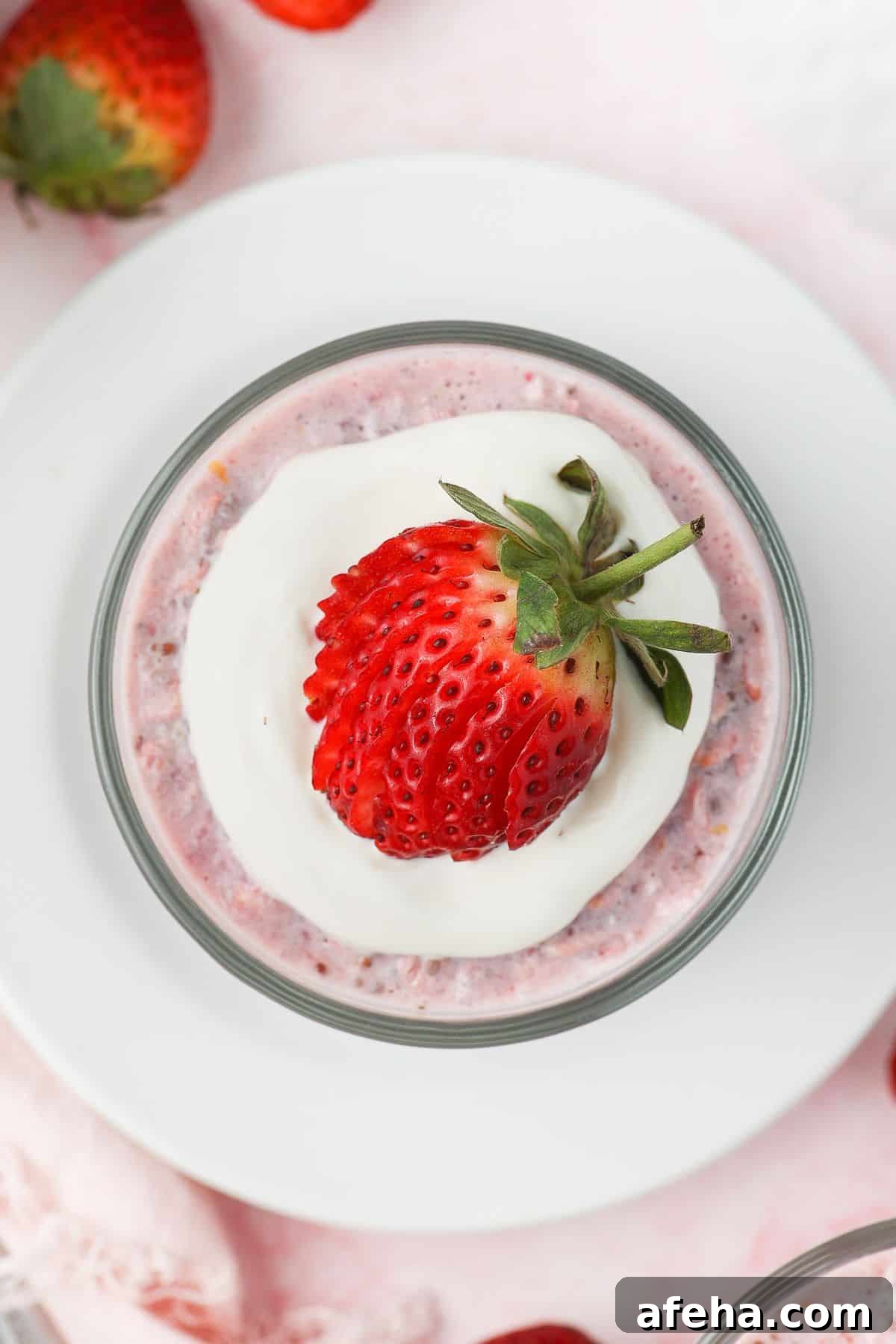 Glass jar of strawberry overnight oats, topped with yoghurt and a strawberry, sitting on a white saucer.