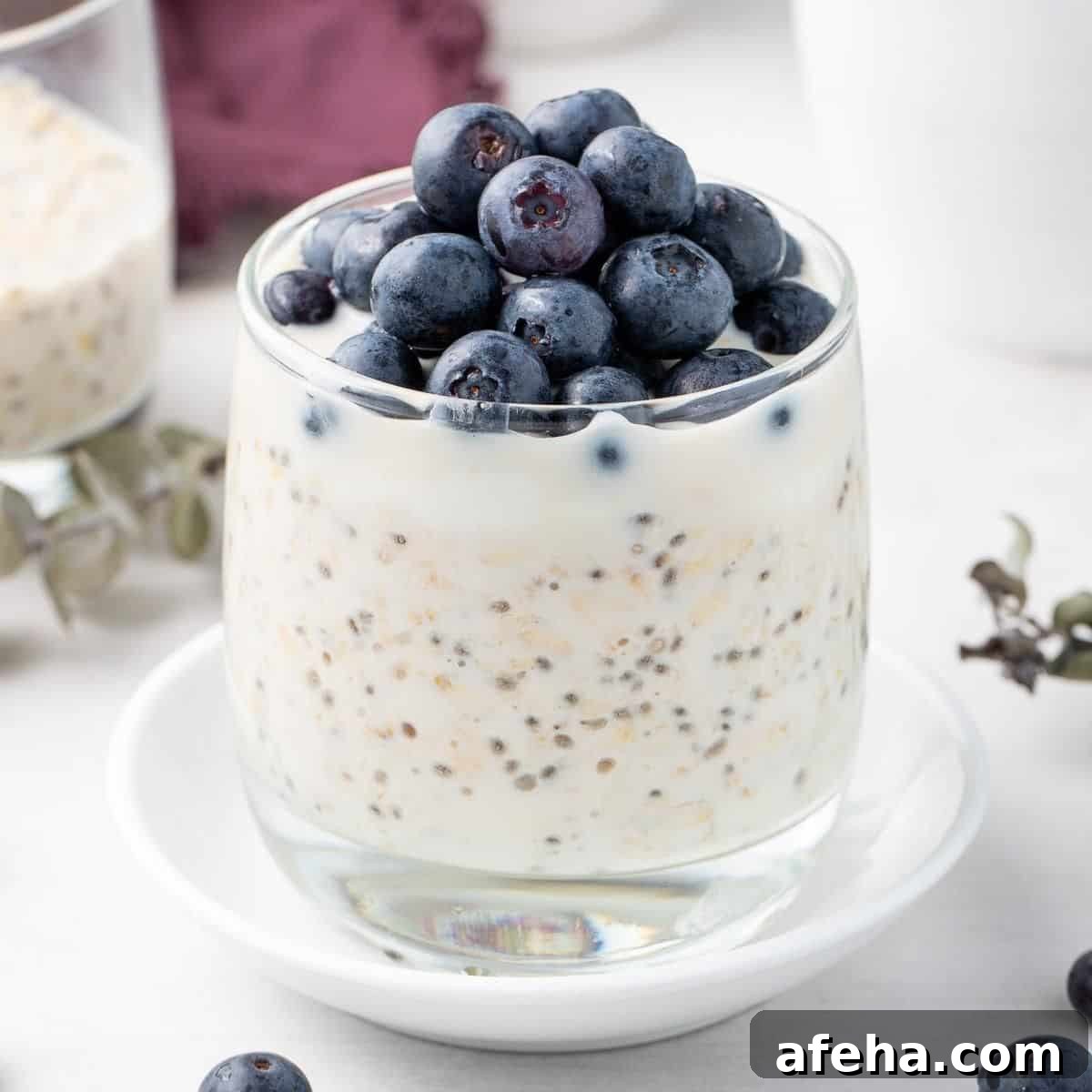 Glass jar of overnight oats topped with yoghurt and blueberries, sitting on a small round white plate.