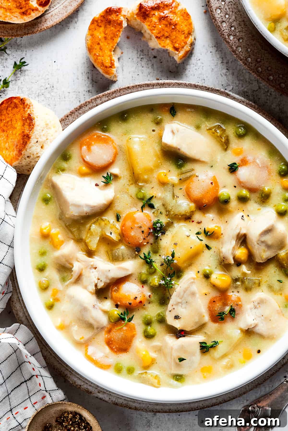 Hearty and comforting chicken pot pie soup has a rich and creamy broth, tender veggies, and juicy chicken, and is so easy to make. Overhead view of a bowl of chicken pot pie soup garnished with thyme, next to some biscuits