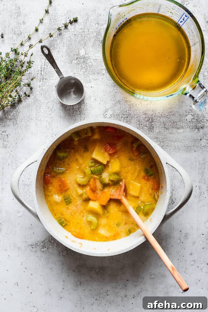 Hearty and comforting chicken pot pie soup has a rich and creamy broth, tender veggies, and juicy chicken, and is so easy to make. A thick veggie soup in a pot with a wooden spoon