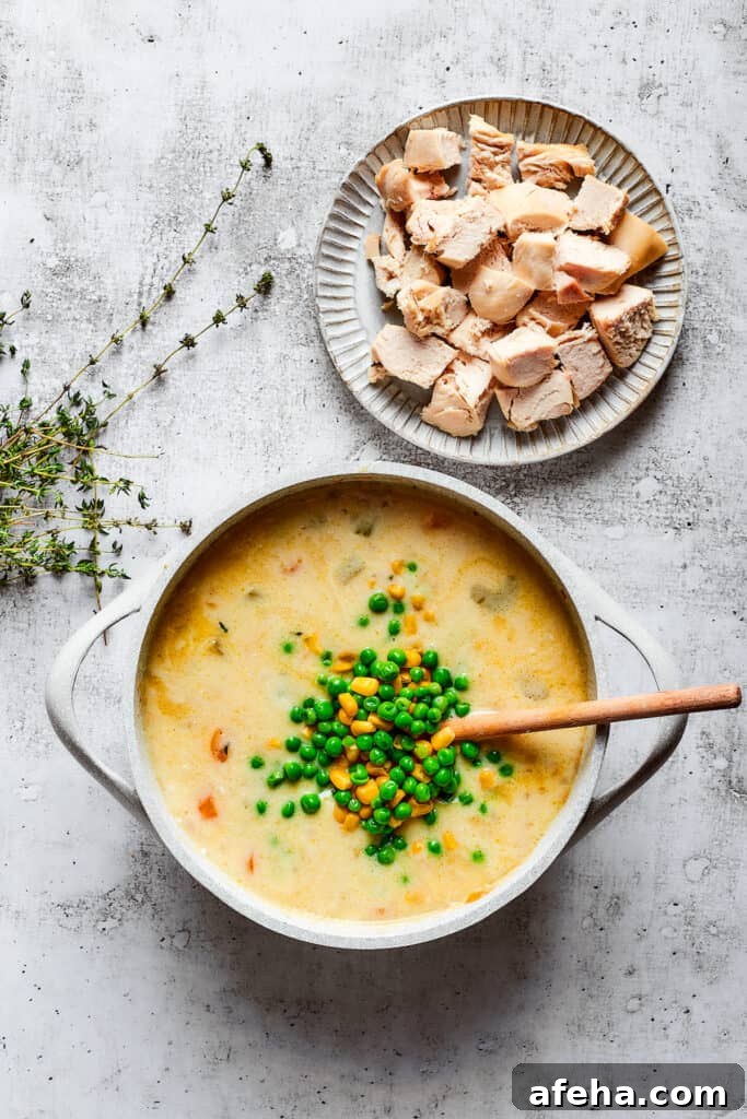 Hearty and comforting chicken pot pie soup has a rich and creamy broth, tender veggies, and juicy chicken, and is so easy to make. A pile of peas and corn on top of a pot of chicken soup