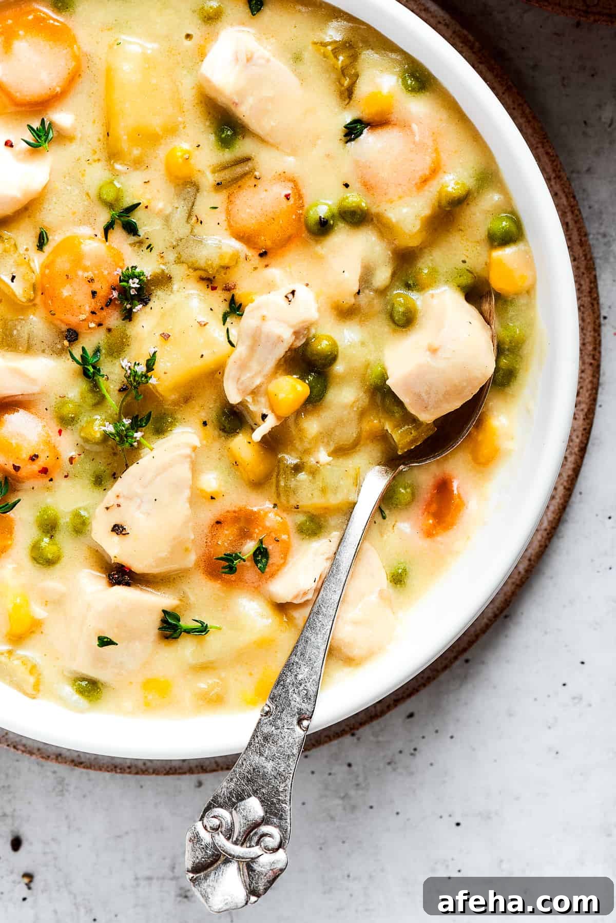 Hearty and comforting chicken pot pie soup has a rich and creamy broth, tender veggies, and juicy chicken, and is so easy to make. Close-up image of a bowl with chicken pot pie soup, topped with thyme, with a spoon resting in the bowl.