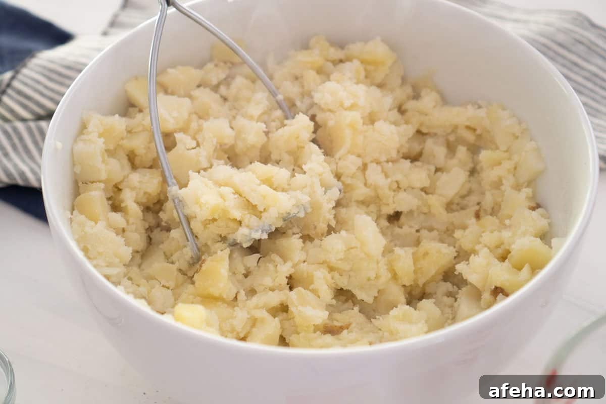 mashing potatoes with potato masher in white bowl