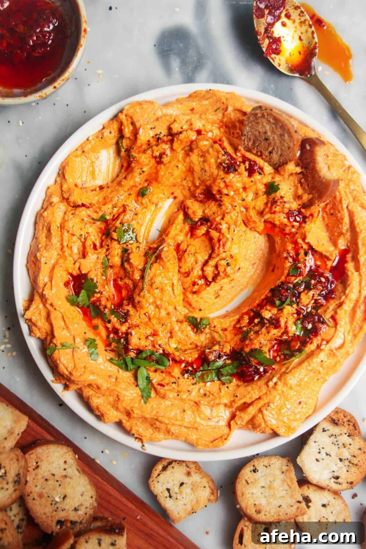 Spicy harissa feta dip on a small white plate, with bagel chips and more harissa on the side.
