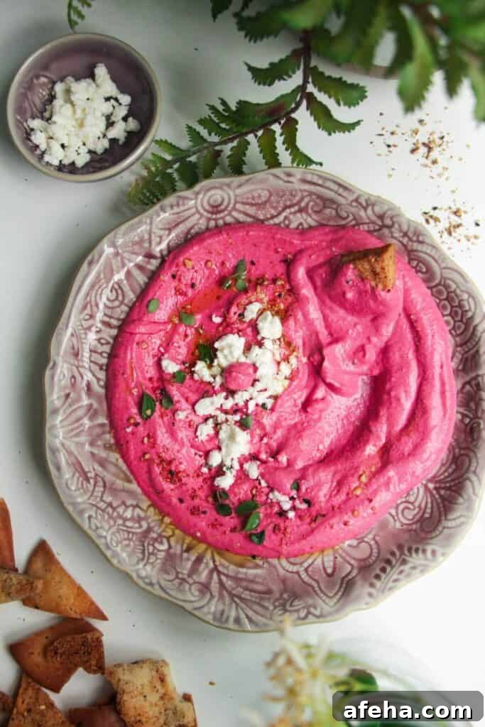 Bright pink beet feta dip on a pink plate with feta crumbled on top and pita chips on the side.