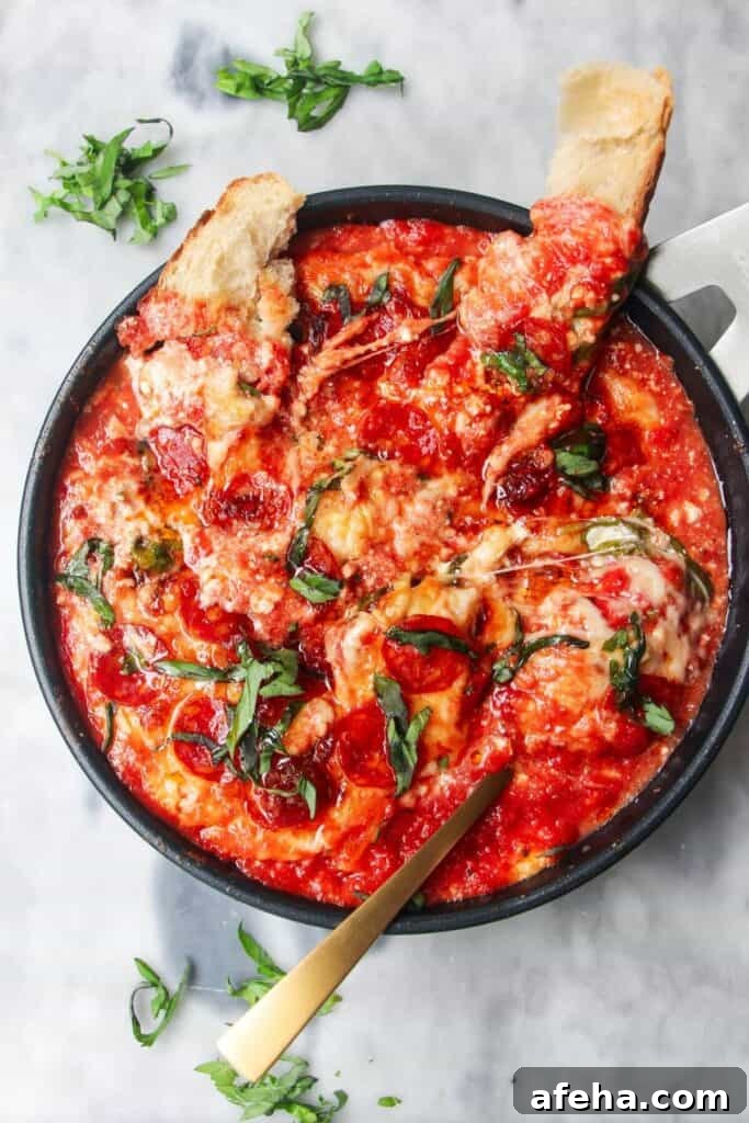 Cheesy pepperoni topped pizza dip with two pieces of bread and a spoon inside.