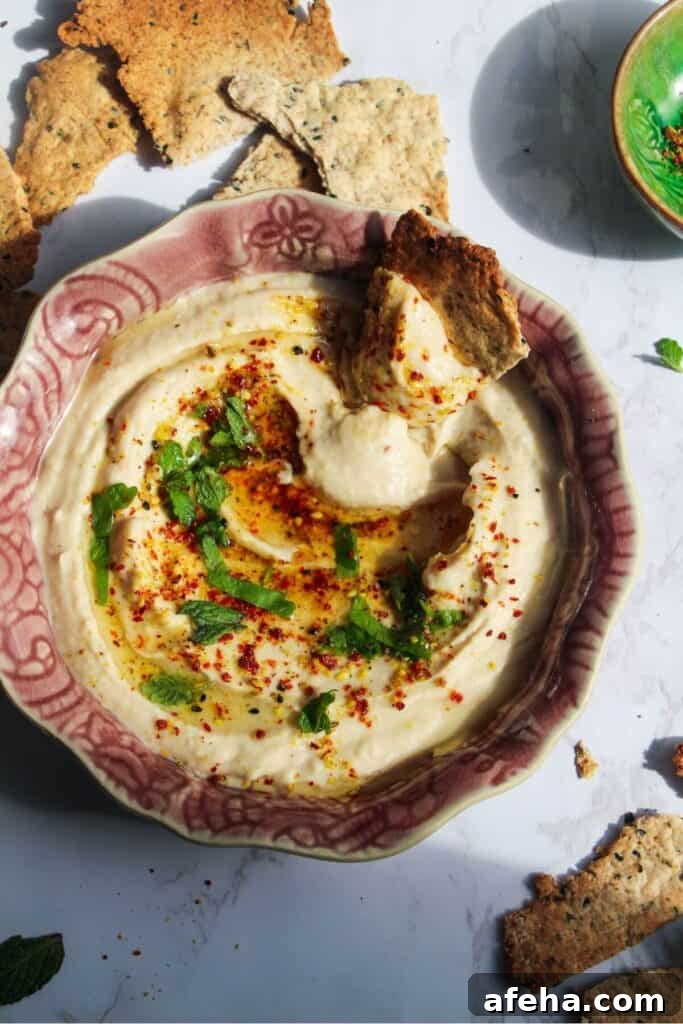 Cracker swirled through white bean dip in a small pink bowl with more crackers on the side.