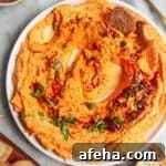 Spicy harissa feta dip on a small white plate, with bagel chips and more harissa on the side.