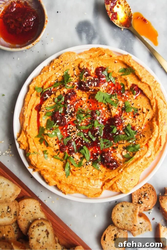 Spicy harissa feta dip on a small white plate, with bagel chips and more harissa on the side.