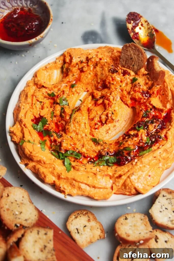 Spicy harissa feta dip on a small white plate, with bagel chips and more harissa on the side.