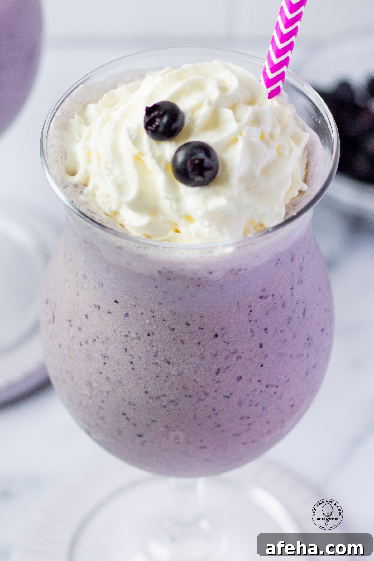 looking down into a glass filled with blueberry milkshake, topped with whipped cream and two fresh blueberries