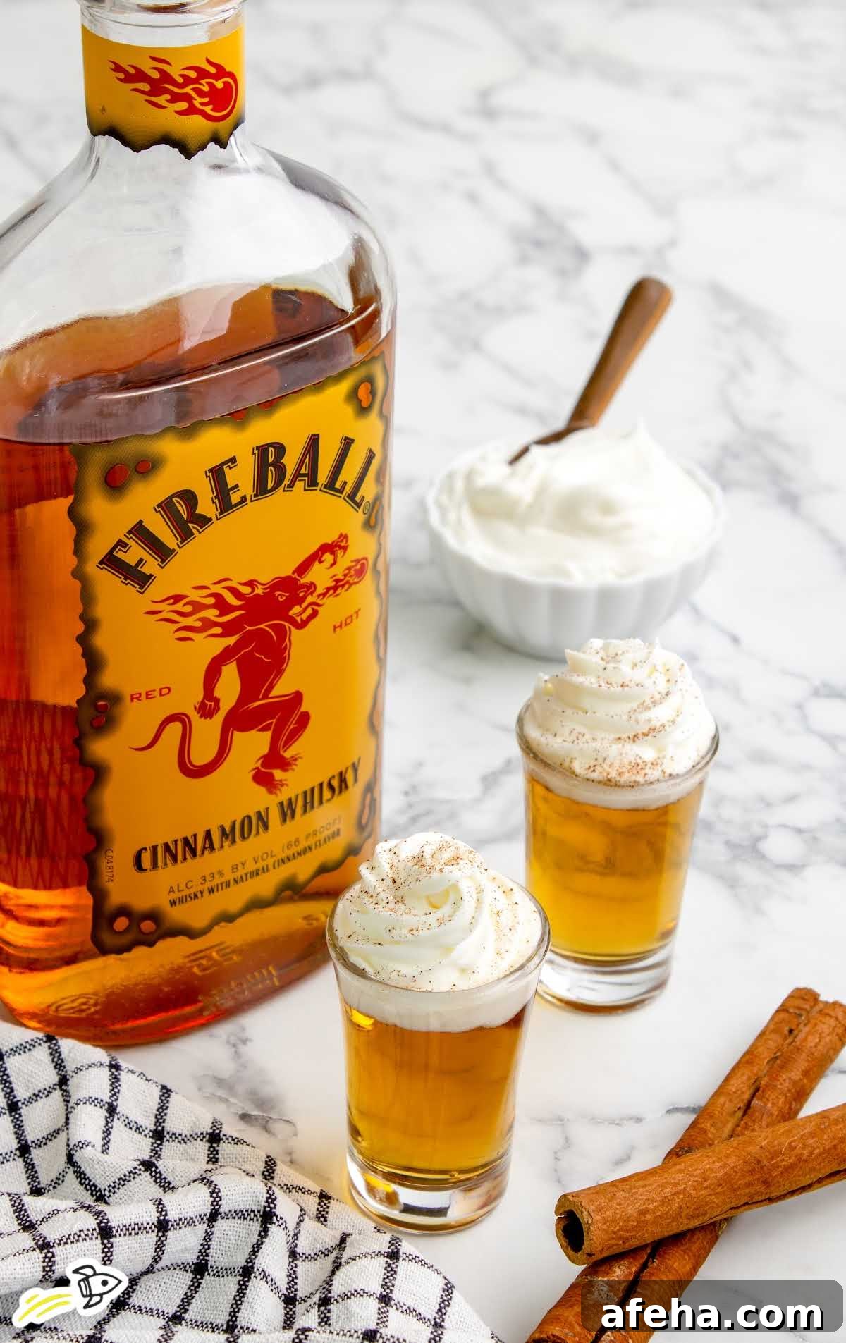 a close up shot of Cinnamon Roll Fireball Shot in cups topped with whipped cream