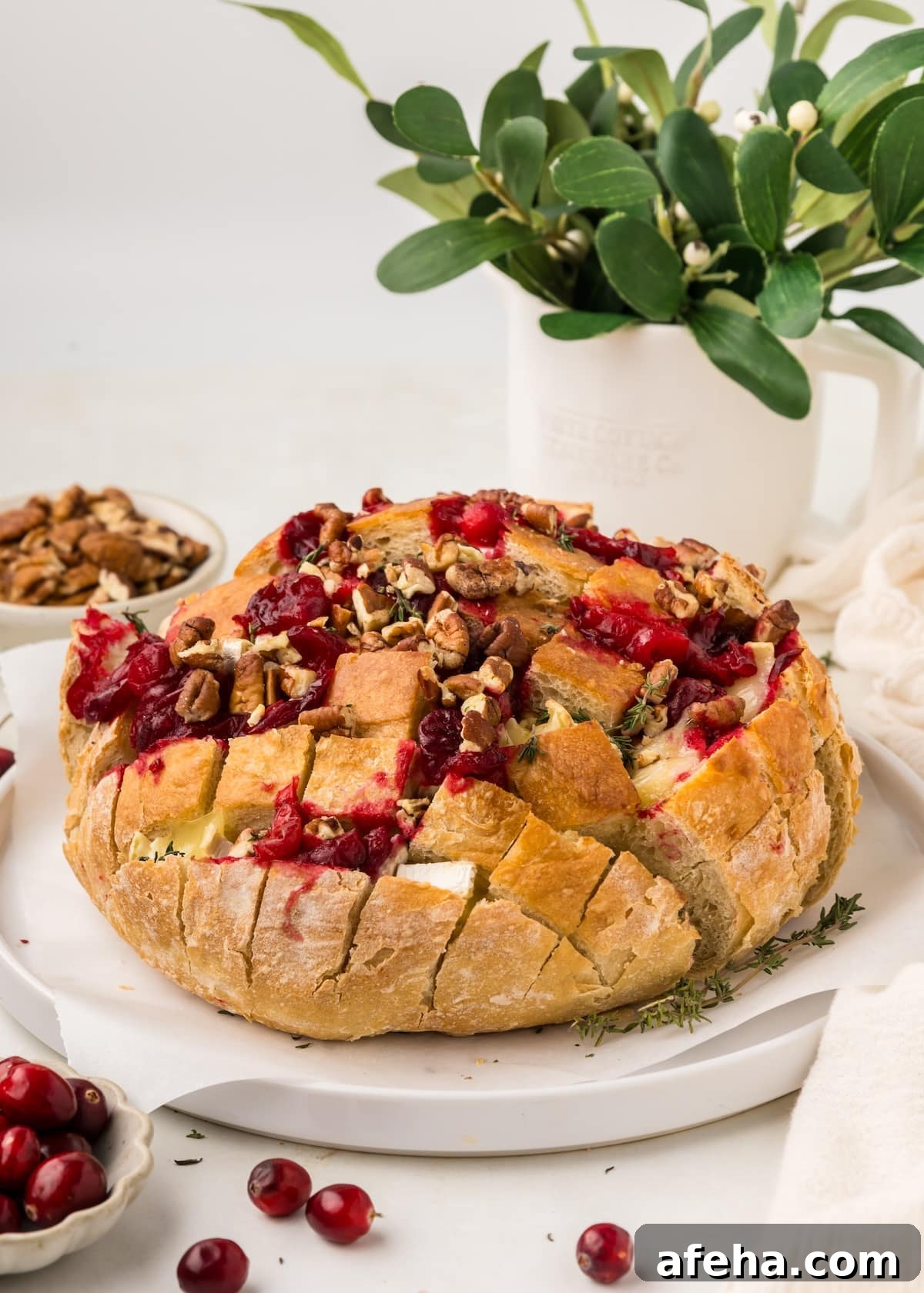 Cranberry Brie Pull Apart Bread on a white plate with fresh cranberries and thyme scattered around it and a vase of greens in the background.