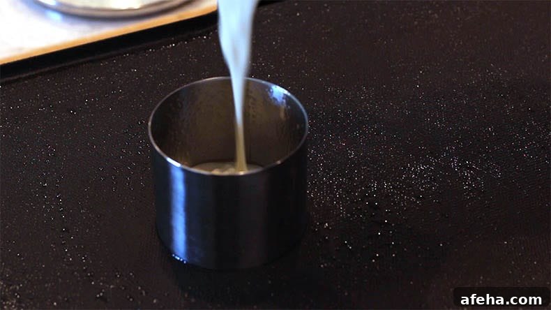 a stainless steel ring on an electric griddle with batter being poured in it