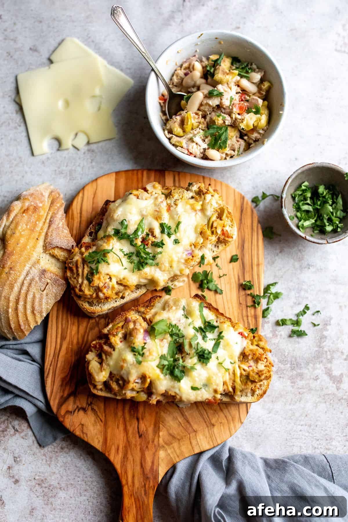 Wooden cutting board and white plate with tuna salad and bread.