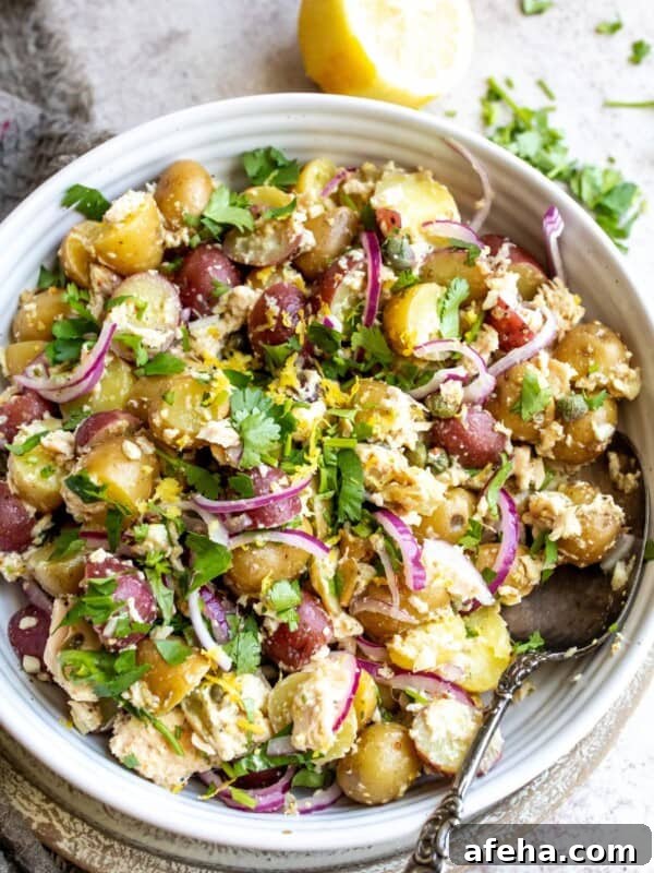 White ceramic bowl with tuna potato salad and silver spoon.