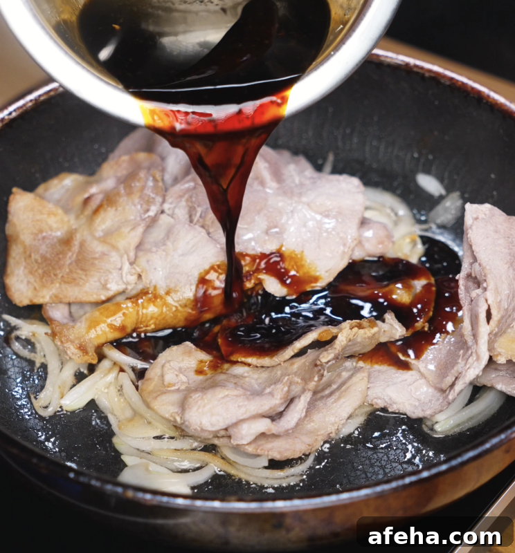 A glossy soy-based sauce is poured over browned pork and sautéed onions in a hot pan, beginning to simmer.