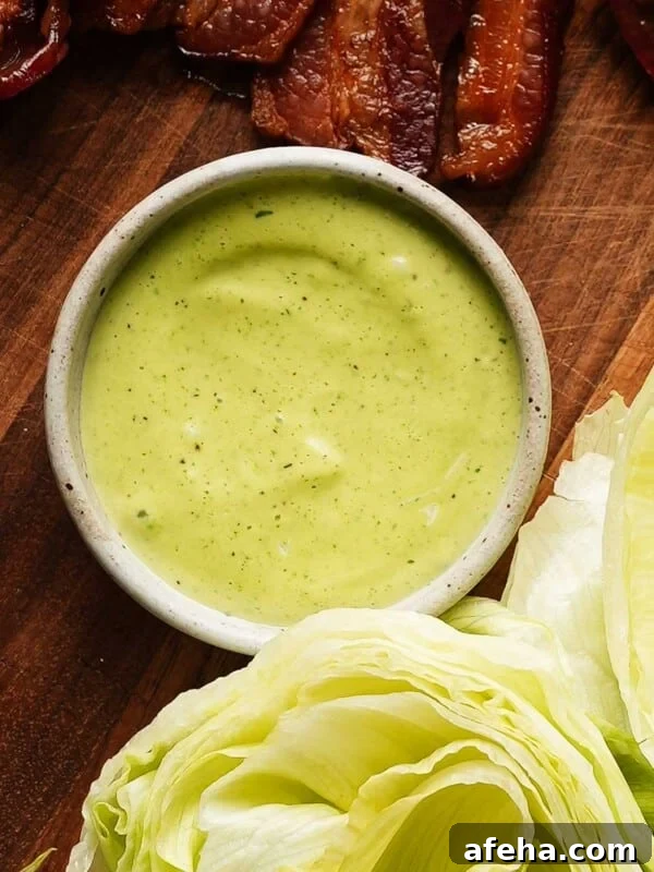 Bowl of basil mayo on wooden board with bacon and lettuce.