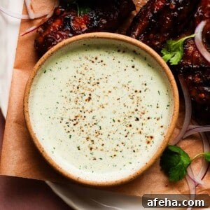 Bowl of creamy ranch garnished with herbs and accompanied by grilled wings.