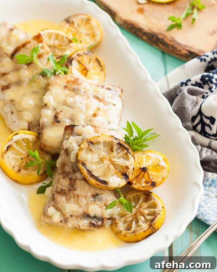 Grilled Mahi Mahi recipe with a lemon butter sauce with sliced lemons on top on a white plate with a turquoise background and a white and blue napkin on the side