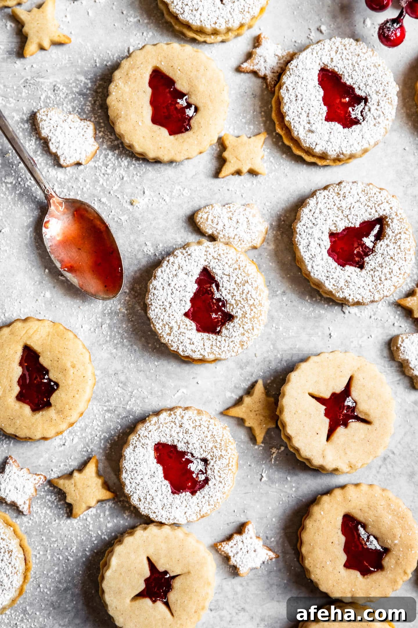Strawberry Cardamom Linzer Cookies dusted with powdered sugar next to a spoon with strawberry preserves on it
