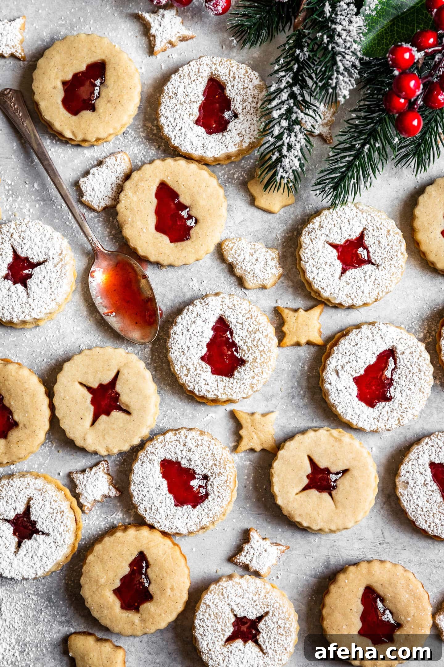 Strawberry Cardamom Linzer Cookies dusted with powdered sugar next to a spoon with strawberry jam on it and festive holiday decor