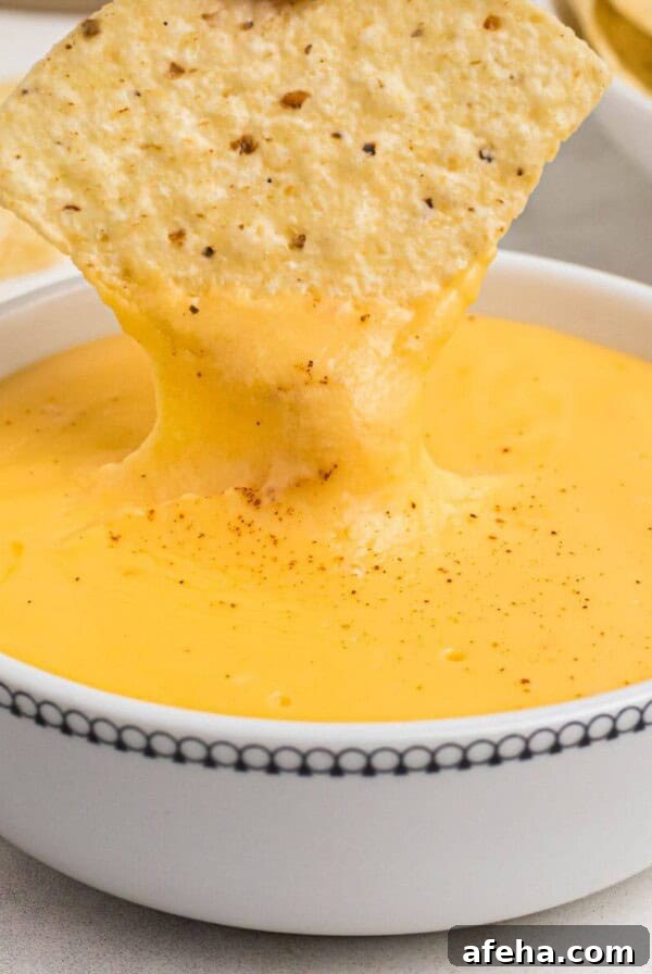 Tortilla chip being dipped into melted cheese in small white bowl.