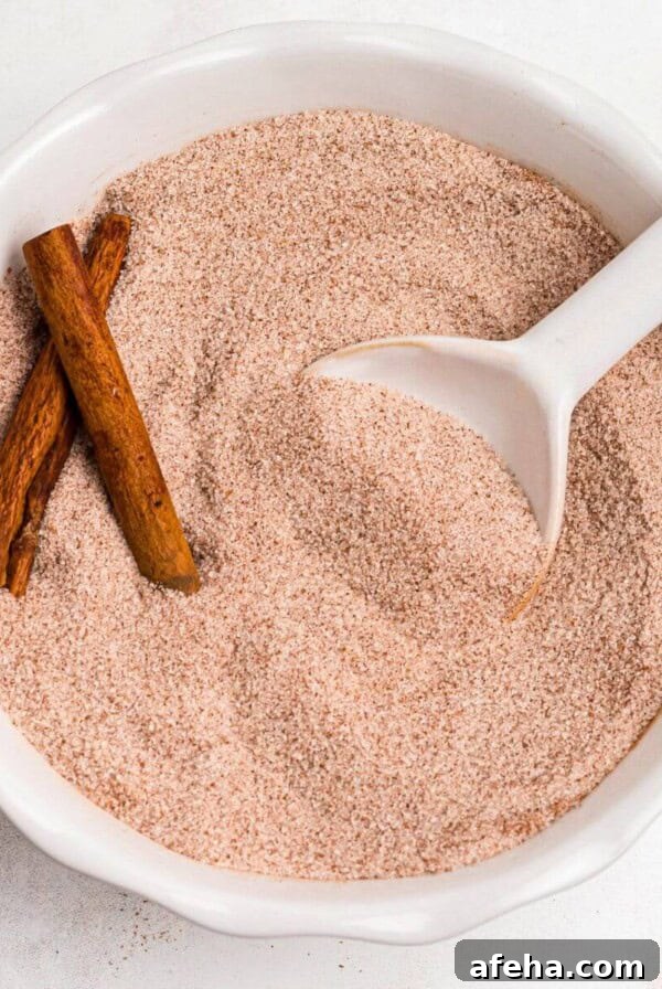Cinnamon sugar mixed in a white bowl with a small white spoon on a marble table.