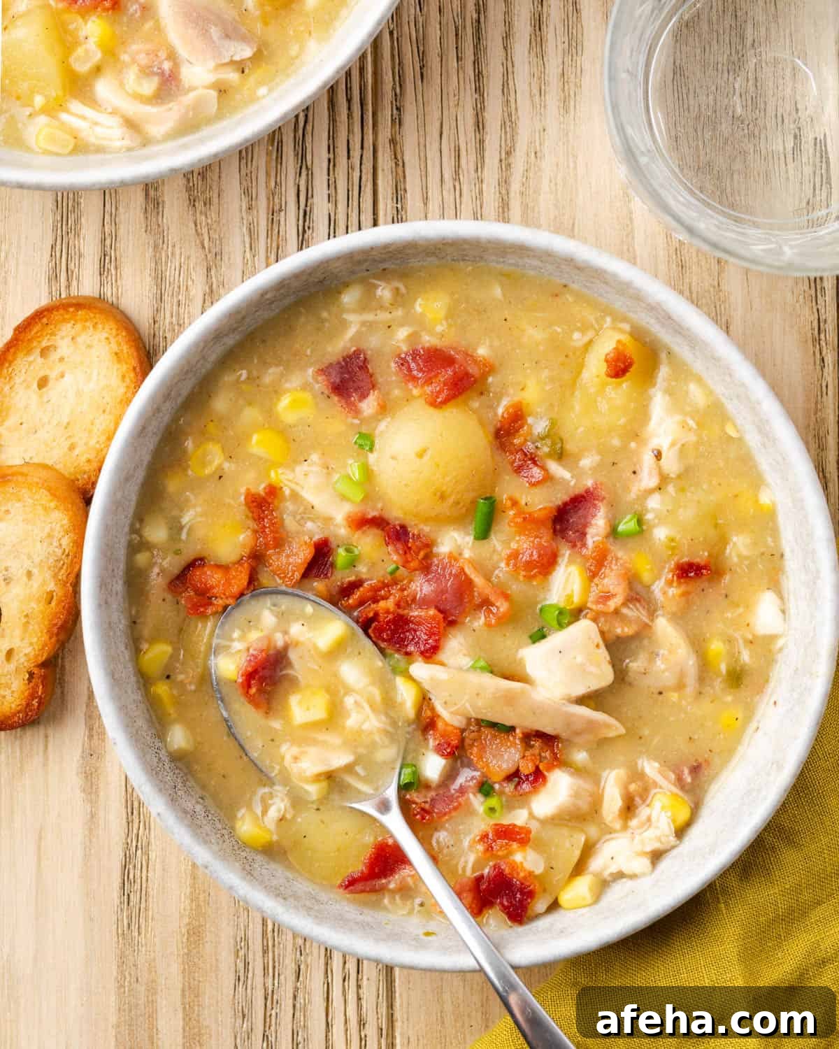 A bowl of chicken corn chowder topped with bacon and chives sitting on a wood table.
