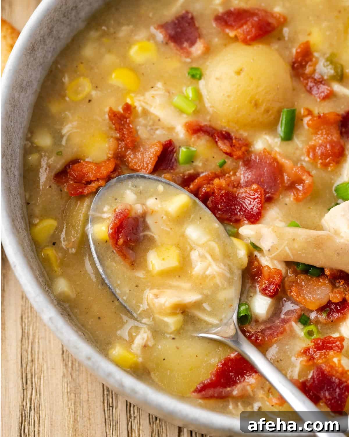 A spoon scooping a bite of chicken corn chowder from a white bowl.