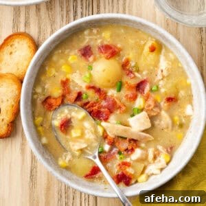 A bowl of chicken corn chowder topped with bacon pieces and chives.