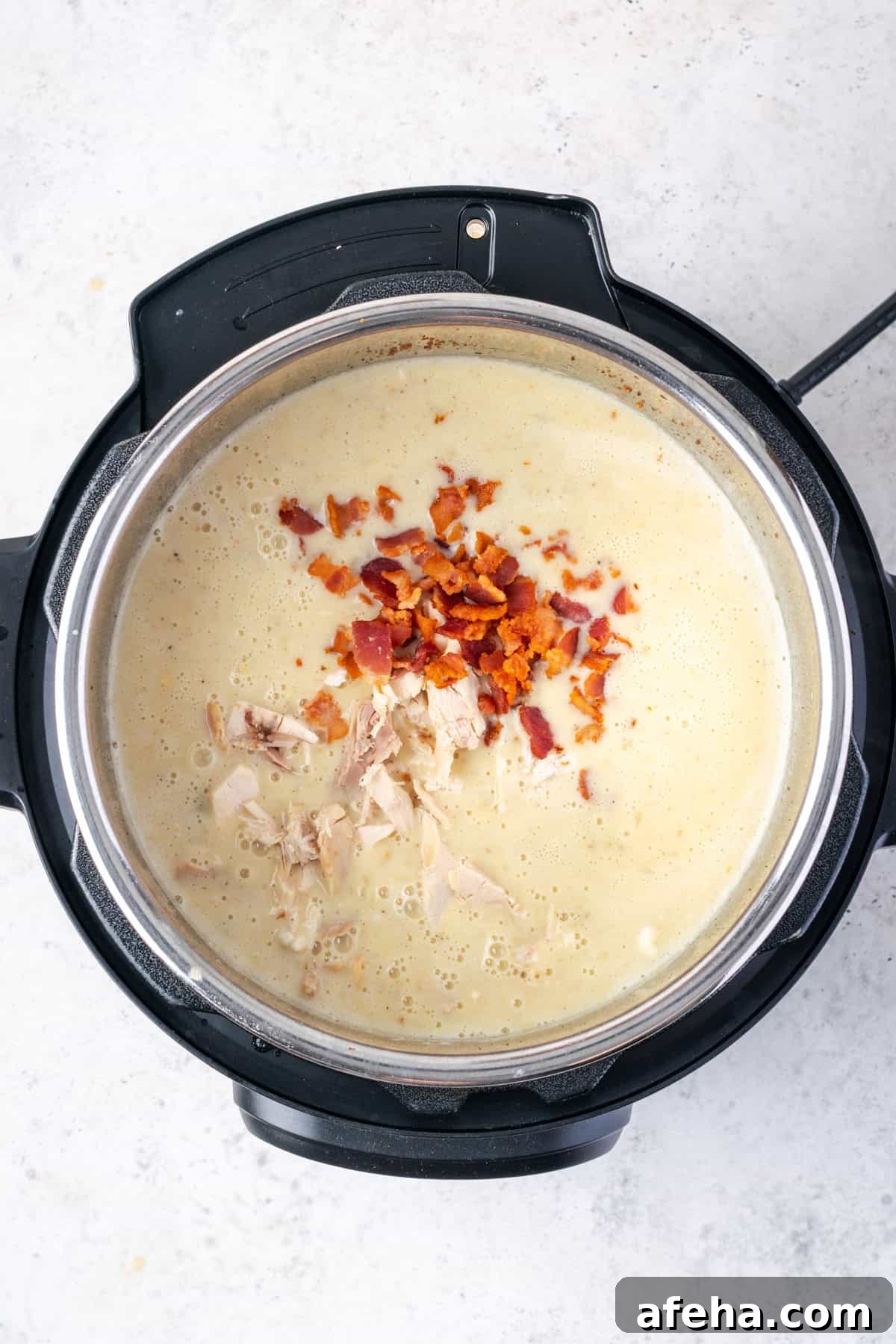 Cooked chicken and bacon pieces being added into the cooked chowder.