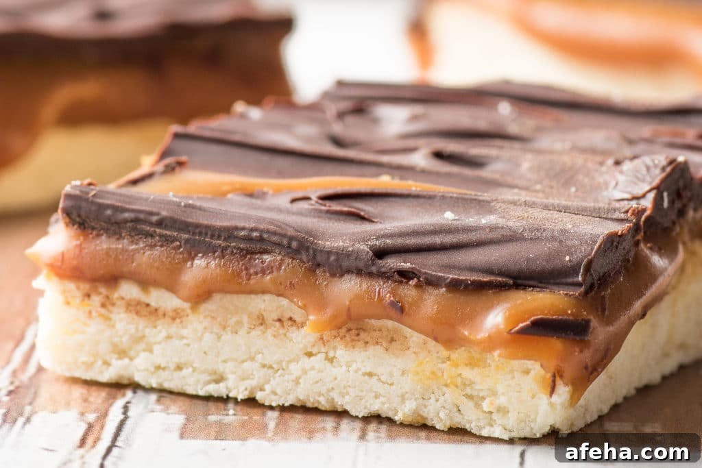 Low carb millionaire bars with gooey caramel filling and dark chocolate crust on a rustic wooden board