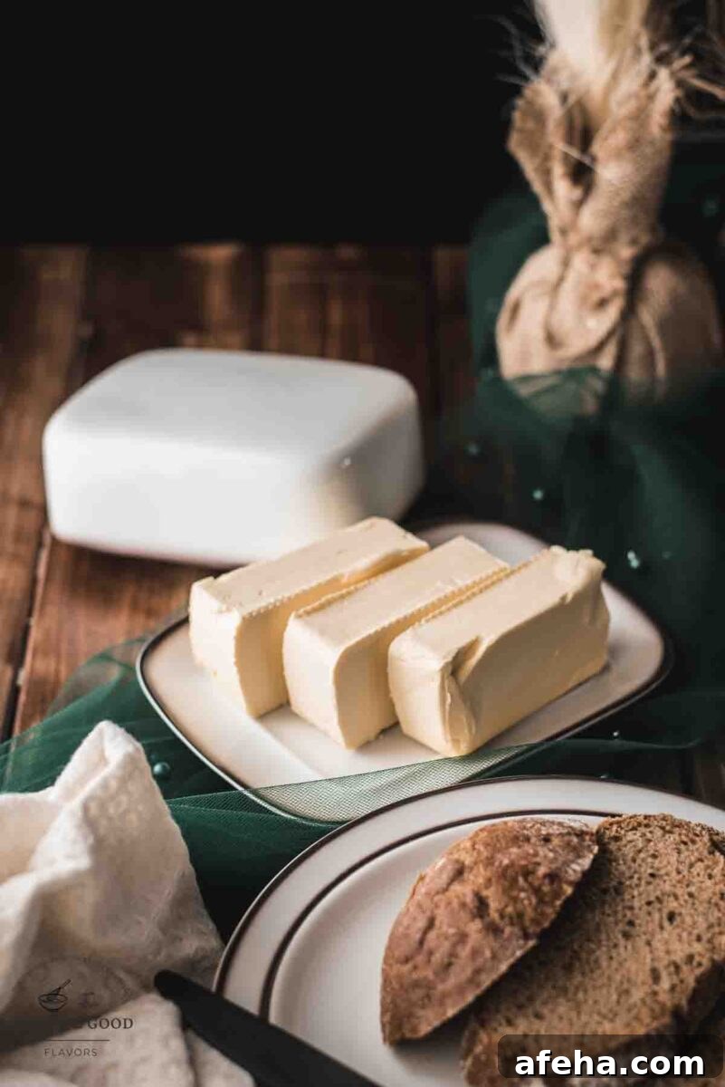 Butter, sliced on white plate with brown colored rim, next to a plate with sliced bread.