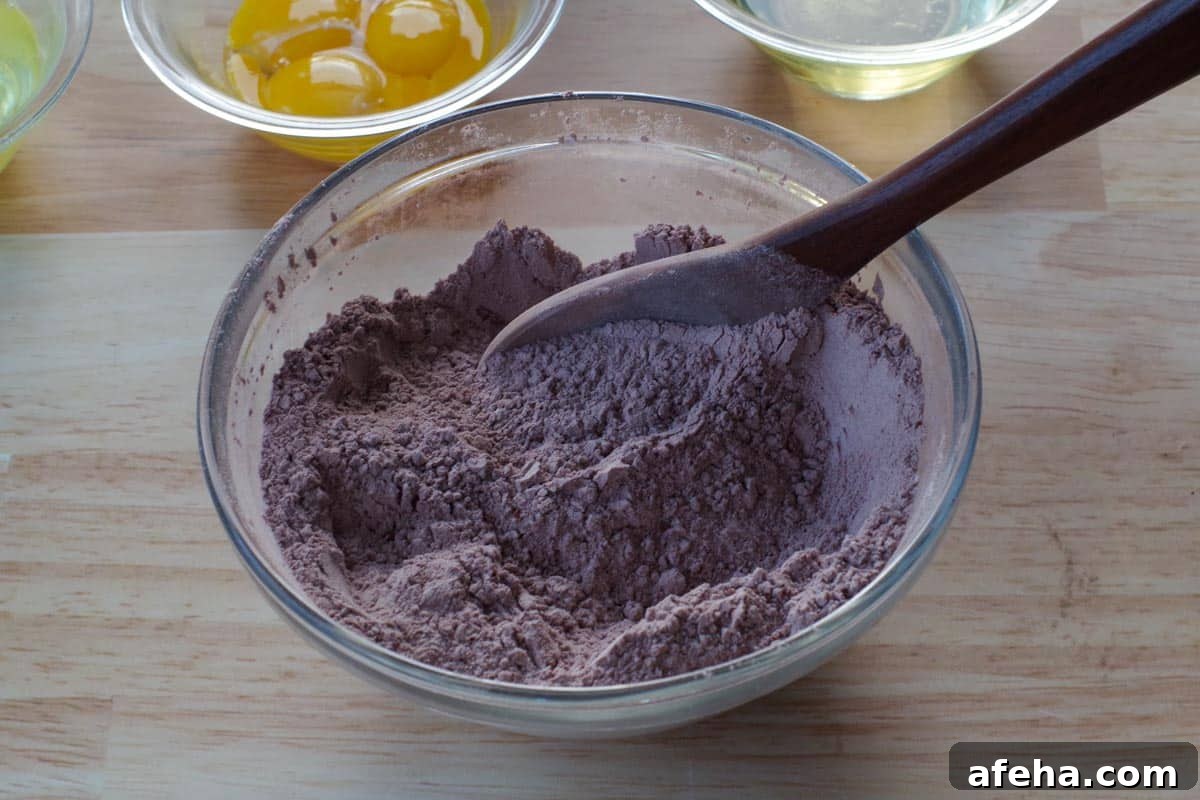 dry ingredients being stirred together in glass bowl, with wooden spoon