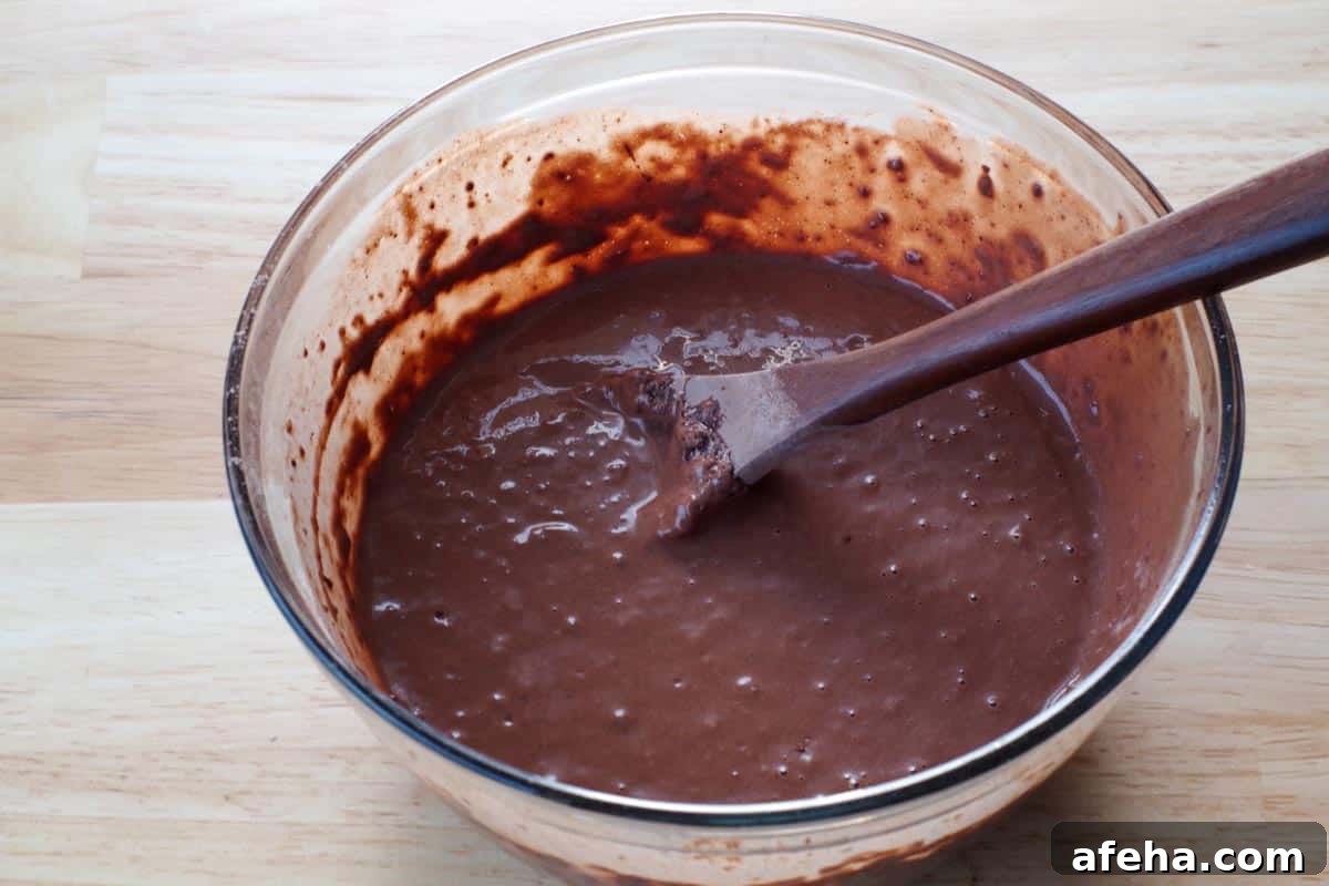 dry ingredients combined with egg yolk mixture in a glass bowl, with wooden spoon