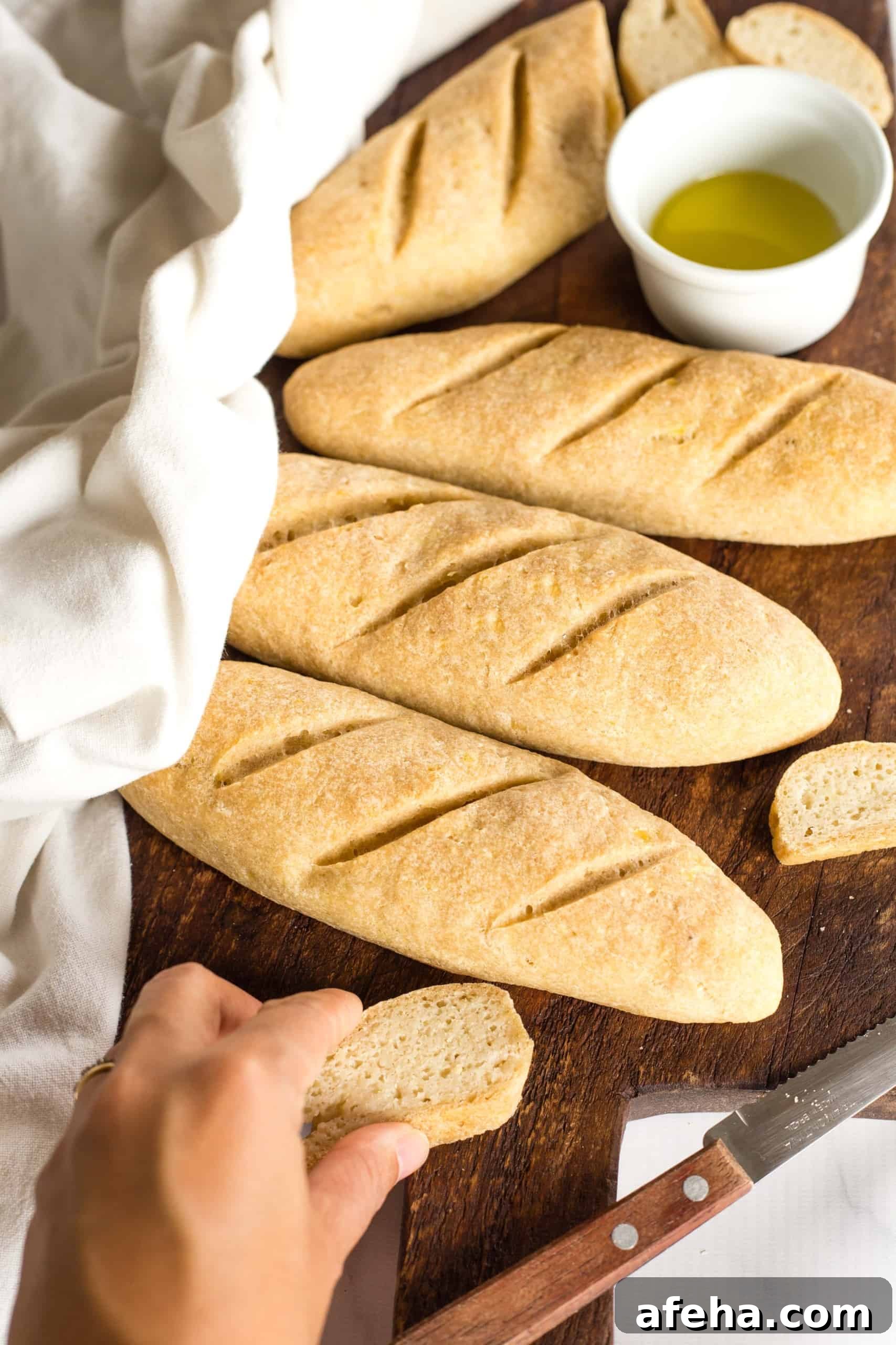 Hand reaching for a slice of gluten-free baguette on board.