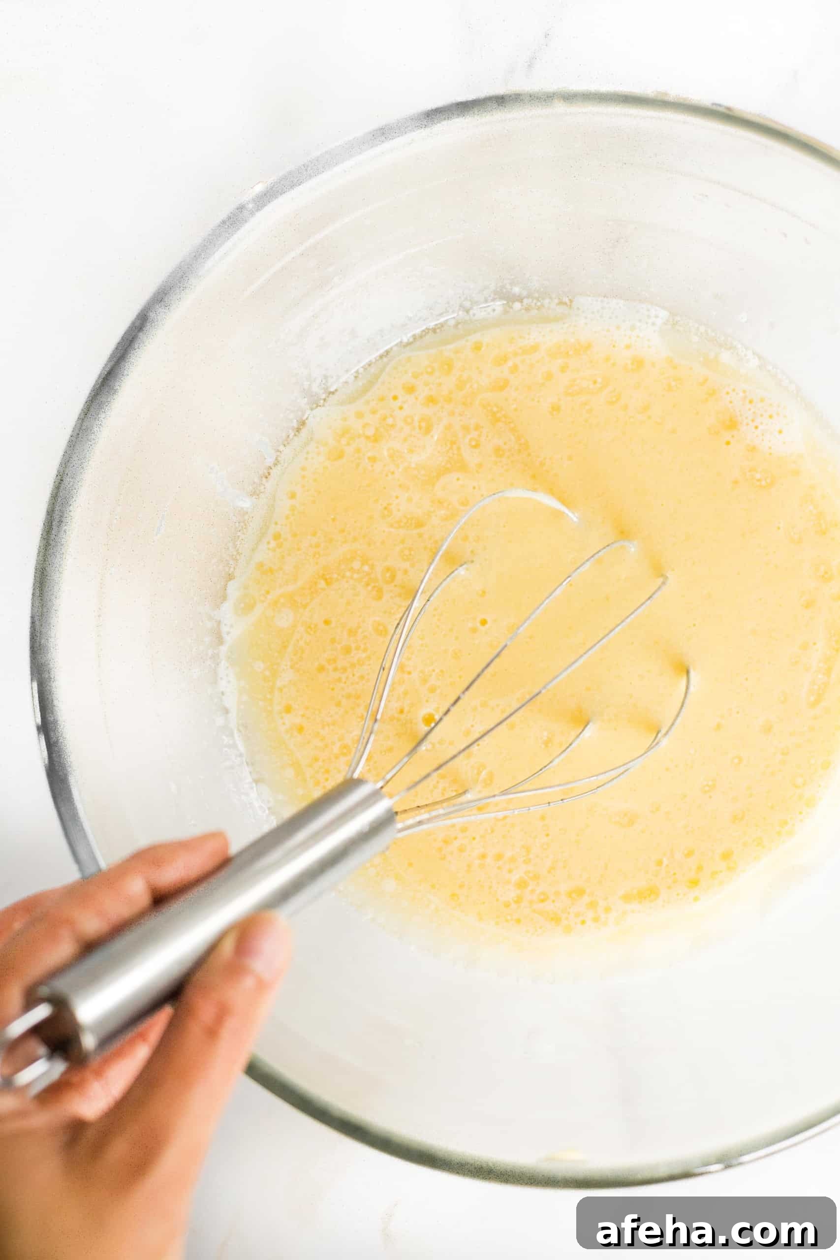 Whisking pale yellow mixture in glass bowl.