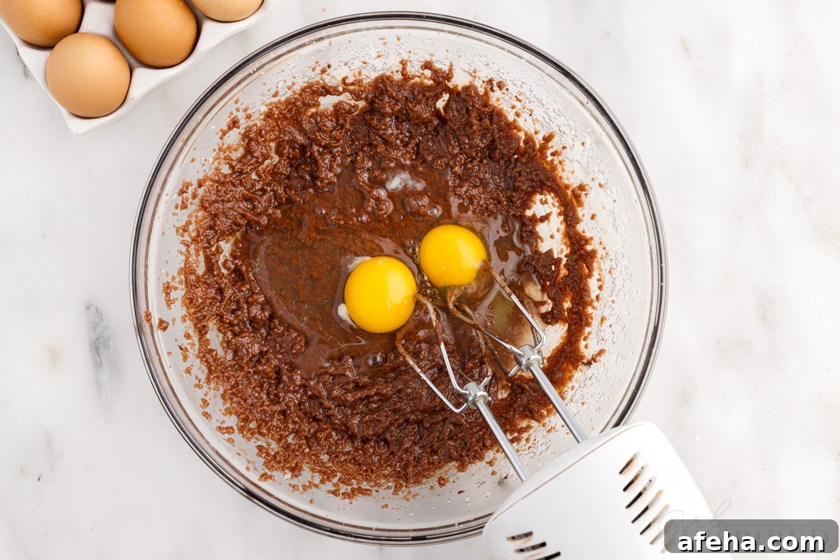 eggs added to chocolate mixture in mixing bowl with mixer next to eggs