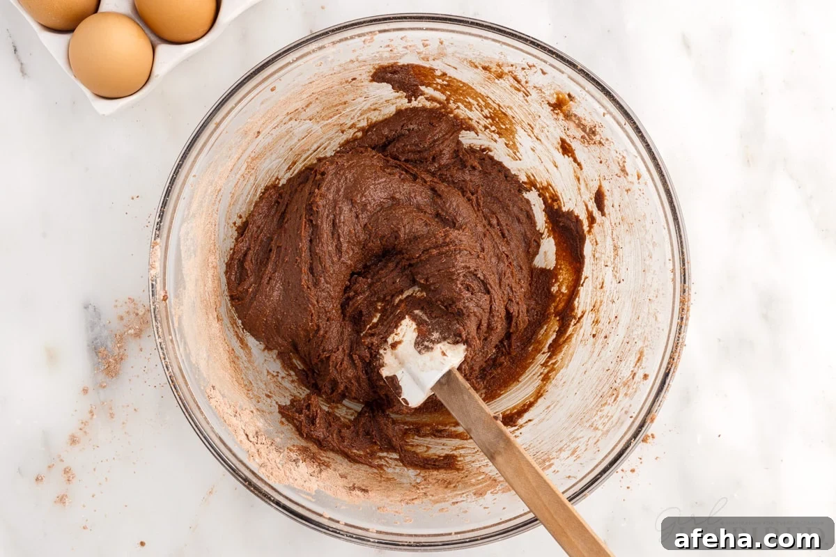 brownie batter mixed together in a mixing bowl with spatula next to eggs