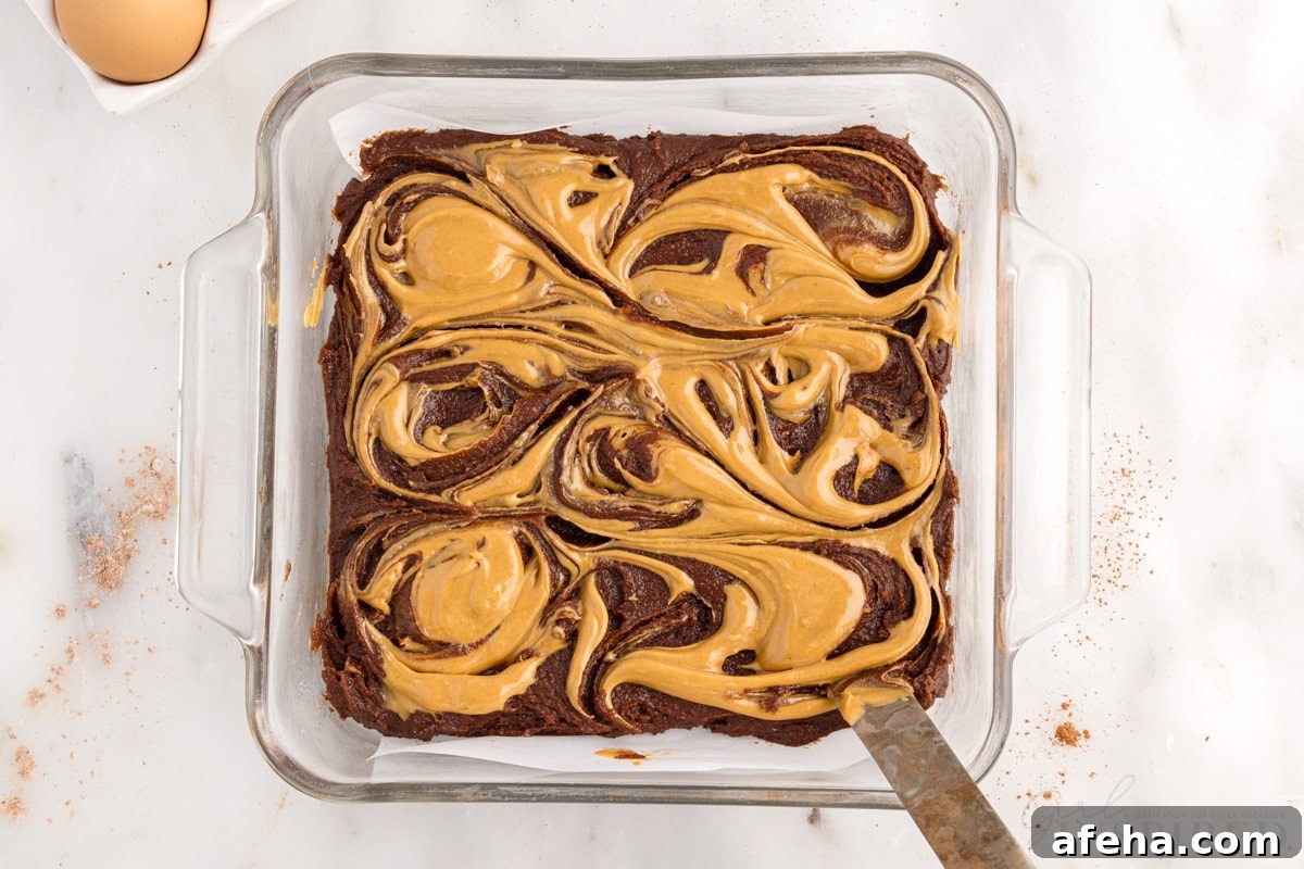 8x8 glass dish with brownie batter and peanut butter swirled into it with knife.