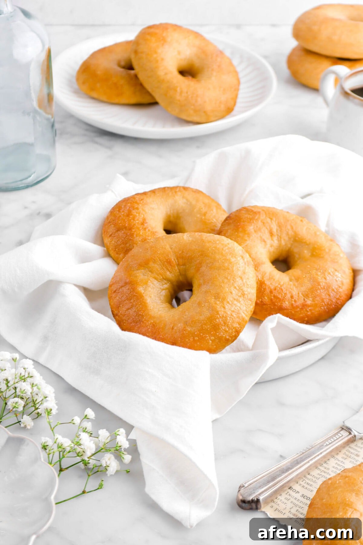 close up o three bagels on white napkin with two bagels on white plate and two more stacked bagels behind