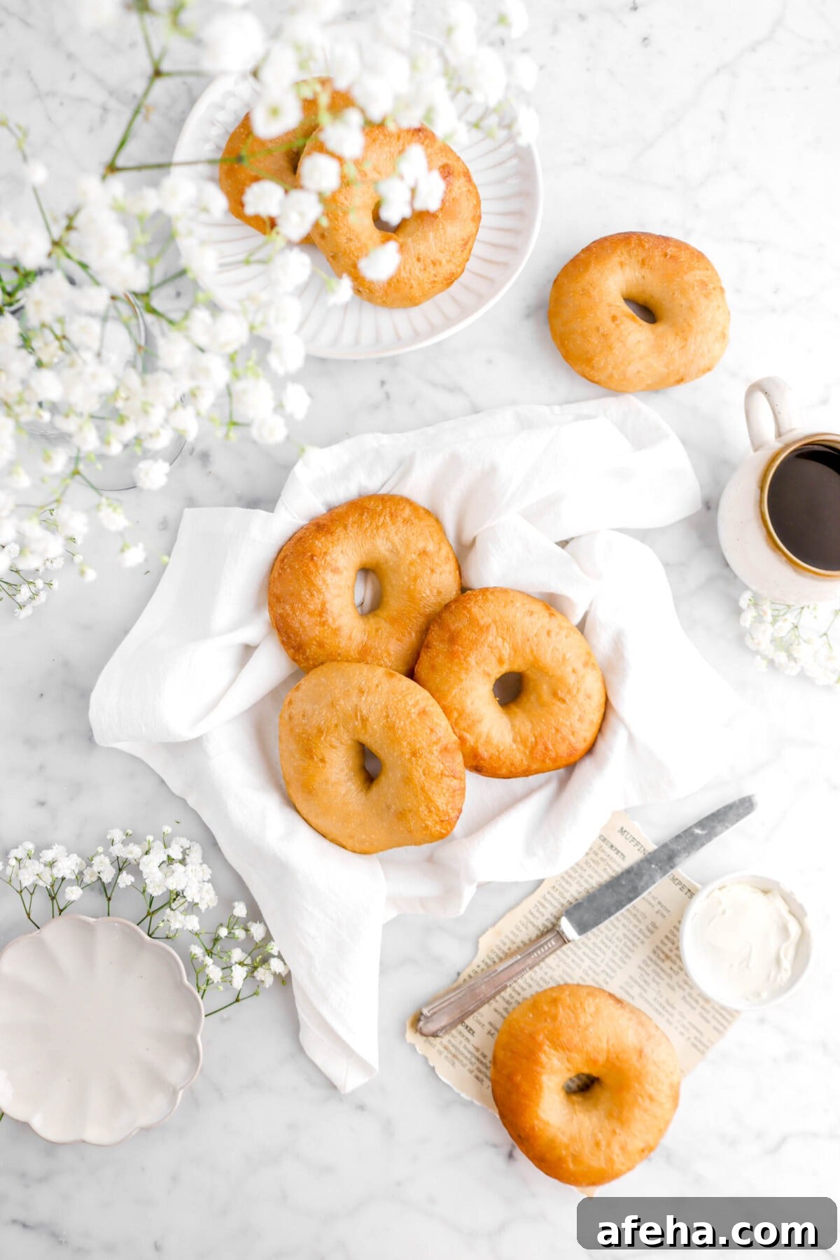 three bagels on white napkin with flowers and other bageks around