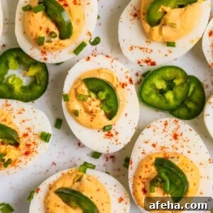 Deviled eggs on white serving dish topped with chopped chives, jalapeño, and paprika.
