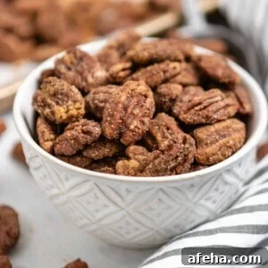 Bowl of candied pumpkin spiced pecans with striped linen and pan behind it.