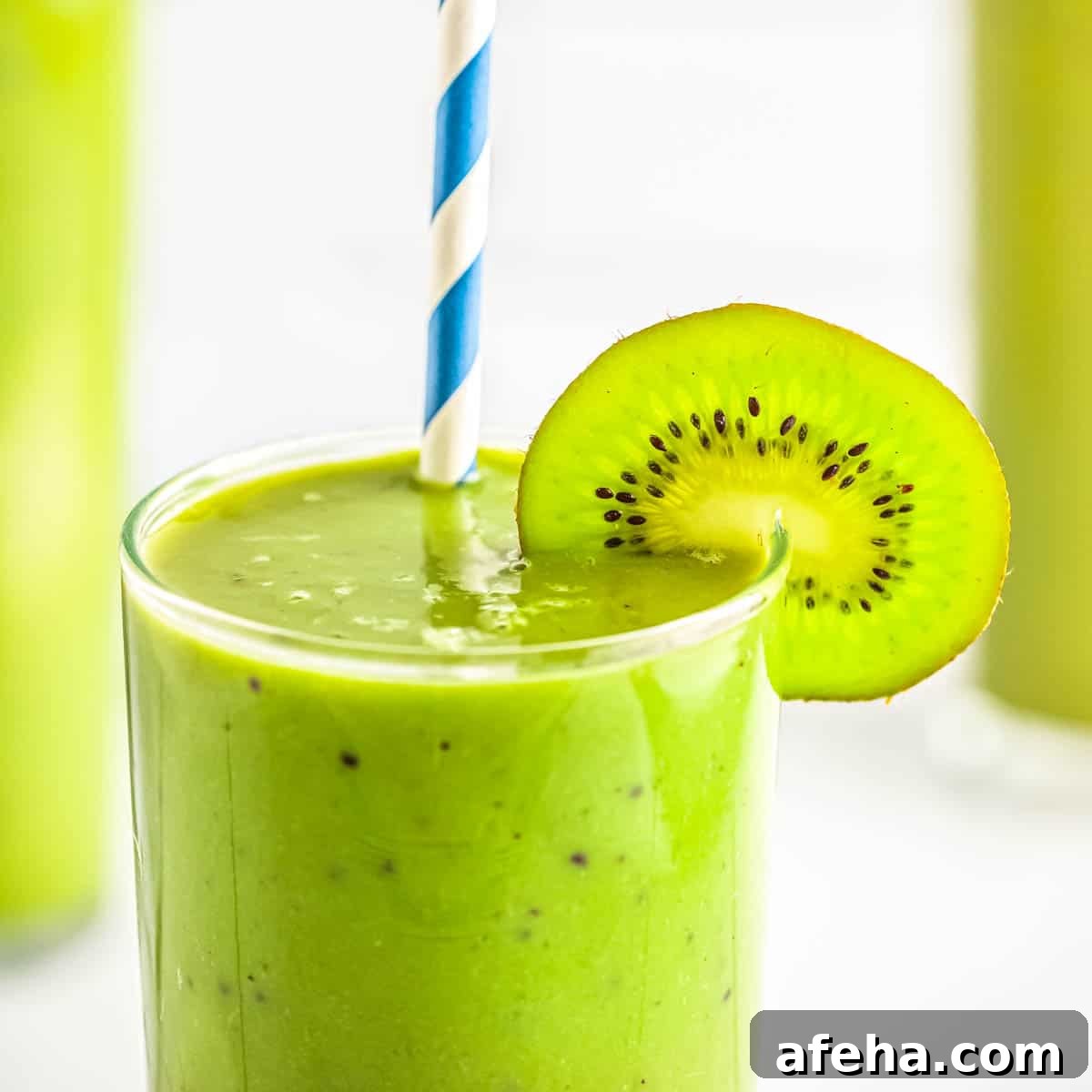 Close up photo of a glass with matcha kiwi smoothie, garnished with a slice of kiwi and a blue and white straw.