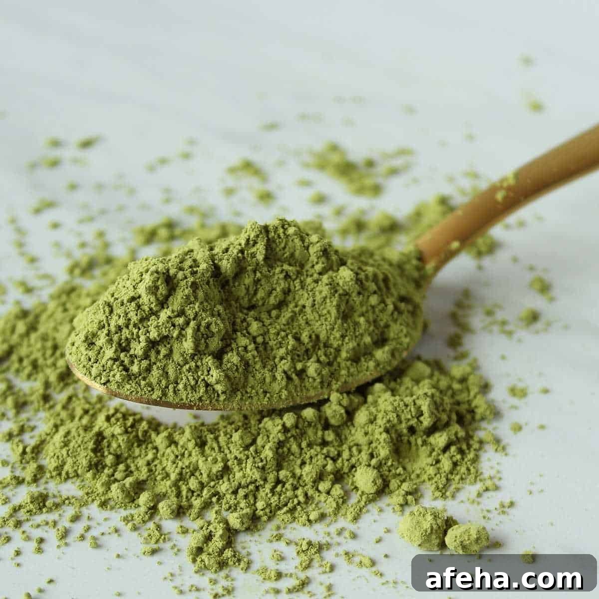 Green tea powder on a wooden spoon spilling over onto a white surface.